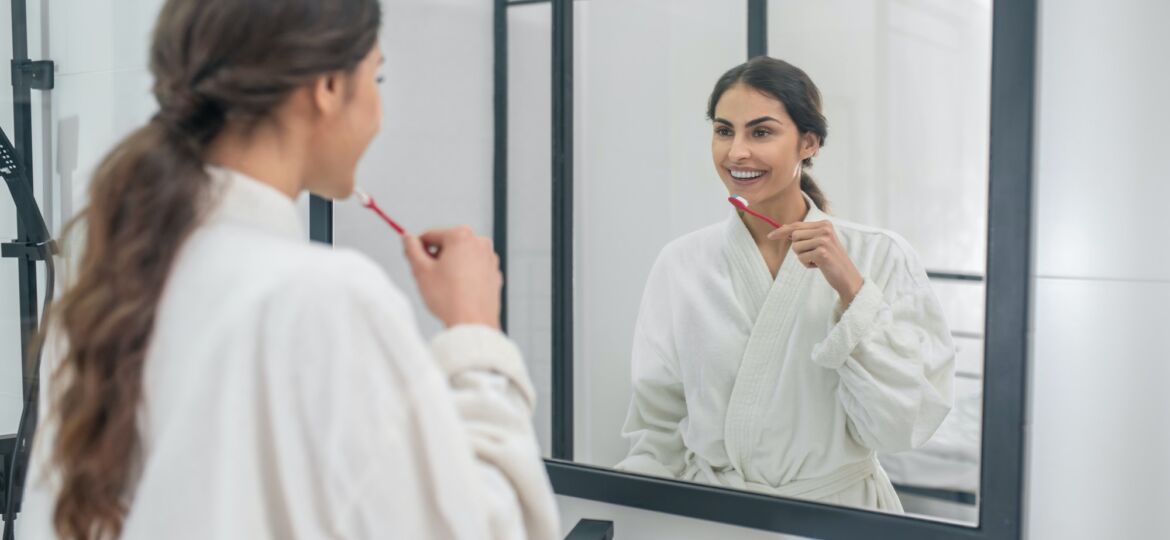 A young pretty woman in a white bathrobe brushing her teeth